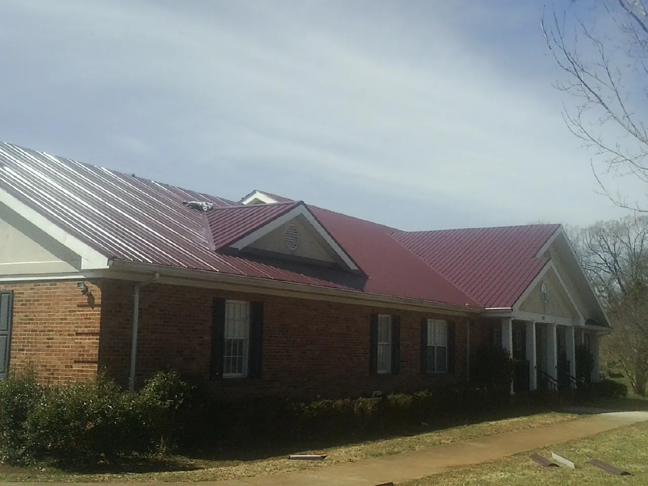 Red metal roof with gabled entries on a long brick building, from a Hail Damage Roof Repair job in Kathleen