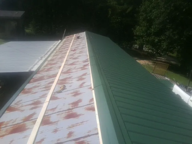 Old rusted panels beside newly installed green metal roofing — Wind Damage Roof Repair by Roofing Brothers in Kathleen